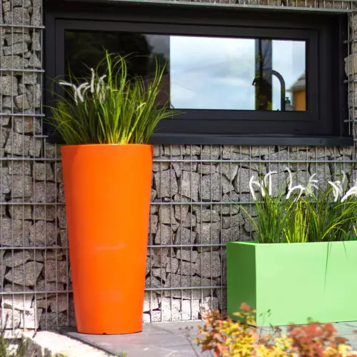 Pomarańczowa donica Habana M w zestawieniu z limonkową donicą Lungo na tle ściany z gabionów