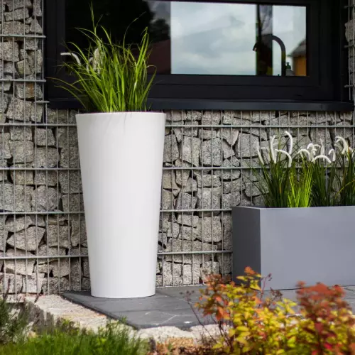 Biała donica Habana M w kompozycji z szarą donicą Lungo na tle ściany z gabionów